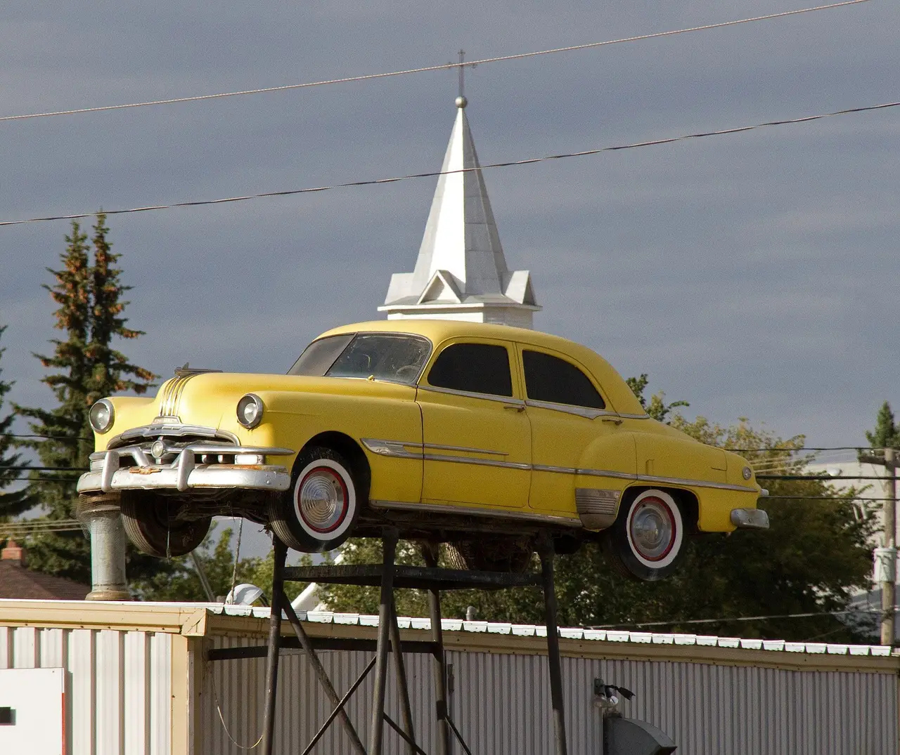Yellow vintage Pontiac on a rooftop stand with church steeple behind, 2012
